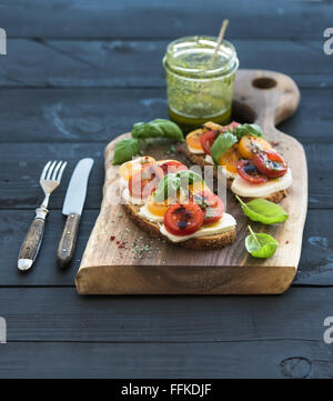 Tomaten, Mozzarella und Basilikum Sandwiches auf dunklen Schneidbrett aus Holz, Glas Pesto auf schwarzem Hintergrund, selektiven Fokus Stockfoto