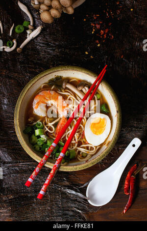 Keramikschale von asiatischen Ramen-Suppe mit Garnelen, Nudeln, Frühlingszwiebeln, in Scheiben geschnitten, Ei und Pilzen, serviert mit roten Stäbchen und ch Stockfoto