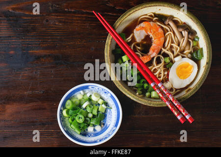 Keramikschale von asiatischen Ramen-Suppe mit Garnelen, Nudeln, Frühlingszwiebeln, in Scheiben geschnitten, Ei und Pilzen, serviert mit roten Stäbchen und sl Stockfoto