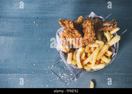 Pommes frites Hähnchenstreifen und Beine mit Pommes frites im Metallkorb über blaue Holztisch mit Meersalz. Ansicht von oben. Mit Retro-filte Stockfoto