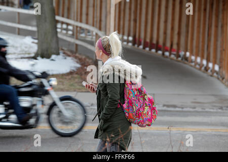 Junge Frau College-Student, Telefon hören, während sie auf die Straße im Winter, geht während ein Motorrad vorbei fährt. Stockfoto