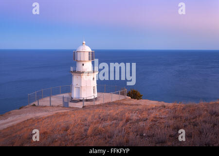 Schönen alten weißen Leuchtturm an der Küste Ozean auf dem Berg bei Sonnenuntergang. Sommer-Seenlandschaft Stockfoto