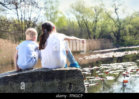 Urlaub-Zeit am Wasser entspannen. Zwei Kinder, ältere Schwester und Bruder sitzen am Ufer des Sees Stockfoto