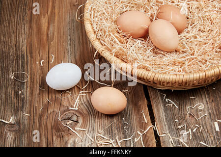 Frische gesunde Ostereier, roh, in ein Osternest mit Stroh auf einem Holztisch. Stockfoto