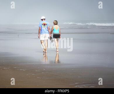 Paar mit ihren Schuhen, walking am Strand an einem nebligen Morgen Stockfoto