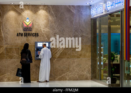 Eine omanische paar an einem Geldautomaten im Wege Shopping-Mall, Muscat, Sultanat Oman Oman Stockfoto