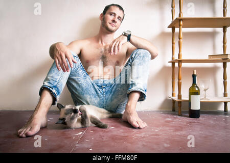 Mann mit einer Flasche Wein und Katze sitzt auf einer Etage Stockfoto