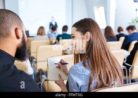 Rückansicht des zwei junge, lächelnde Menschen, schreiben und sprechen auf Business-Meeting im Konferenzsaal Stockfoto