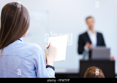 Rückansicht der junge Geschäftsfrau schreiben und Notizen im Editor auf öffentlichen Presetration im Konferenzsaal sitzen Stockfoto