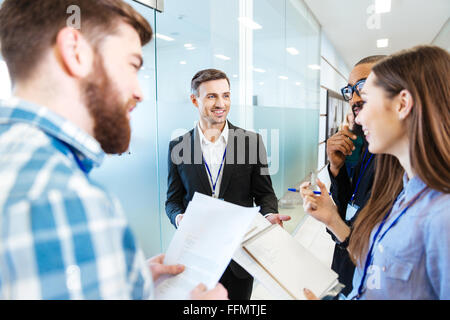 Gruppe von lächelnden jungen Menschen stehen und reden mit Teamleiter in der Halle des Büros Stockfoto