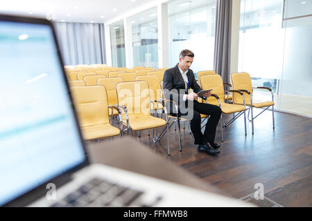 Nachdenklich konzentrierte Geschäftsmann sitzt und mit Tablet im leeren Saal Stockfoto