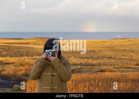 Eine Frau nimmt ein Bild an einem sonnigen Nachmittag auf Snaefellsjoekull Halbinsel, Island, mit einer Diana Kamera und der Regenbogen hinter Stockfoto