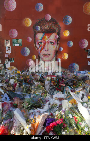 Blumen unter einem David Bowie "Aladdin Sane" Wandbild auf einer Straße Wand in Brixton, nach seinem Tod in einem behelfsmäßigen Schrein gemacht. Stockfoto