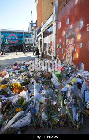 Blumen unter einem David Bowie "Aladdin Sane" Wandbild auf einer Straße Wand in Brixton, nach seinem Tod in einem behelfsmäßigen Schrein gemacht. Stockfoto