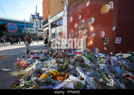 Blumen unter einem David Bowie "Aladdin Sane" Wandbild auf einer Straße Wand in Brixton, nach seinem Tod in einem behelfsmäßigen Schrein gemacht. Stockfoto