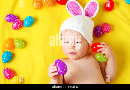 Baby Boy in Hase Hut liegen auf gelbe Decke mit Ostereiern Stockfoto