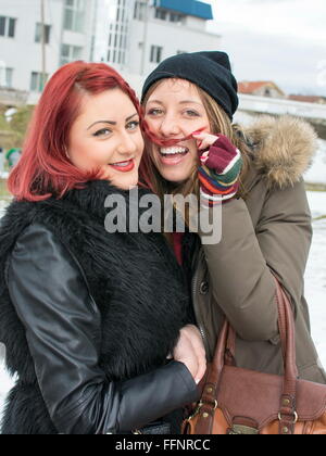 zwei Mädchen, die Spaß in das Winterwetter, ist ein Mädchen einen Schnurrbart mit ihren Haaren machen. Stockfoto