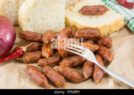 kleine hausgemachte Würste auf ein Stück Packpapier mit Brot Gemüse und Besteck Stockfoto