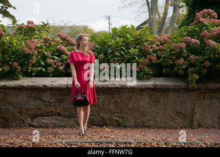 Schöne blonde Frau im roten Kleid mit einem Vintage Auftritt warten auf dem Bürgersteig. Stockfoto