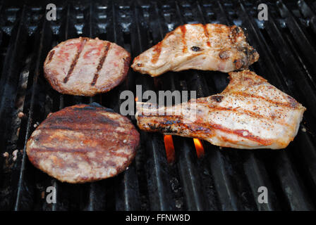 Schweinekoteletts und Hamburger Pastetchen Kochen auf dem Grill Stockfoto