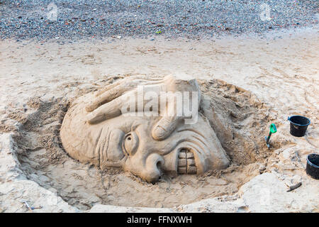 Sandskulpturen von einer hässlichen Kopf am Südufer des Bahndamms bei Ebbe, Themse, London, UK, gebaut für Tipps Stockfoto