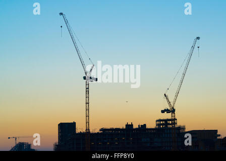 Silhouetten von zwei massiven Baukräne mit Himmel bei Sonnenuntergang im Hintergrund. Stockfoto