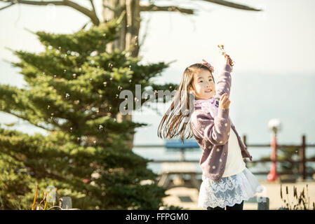 Asien, das Kind bläst einen Löwenzahn in einem Park. Stockfoto