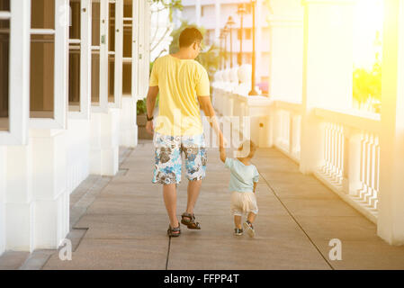 Rückansicht von Vater und Sohn Hand in Hand gehen im Sonnenuntergang. Elternteil und Kind in den Urlaub. Stockfoto