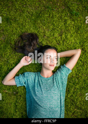 schöne junge Frau liegt auf grünem Moos Entspannung mit Hände hinter seinem Kopf lächelnd Stockfoto