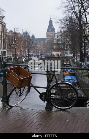 Fahrrad angekettet an Geländer an einem Kanal in Amsterdam, die Niederlande, auf einem nassen und regnerischen Tag im winter Stockfoto