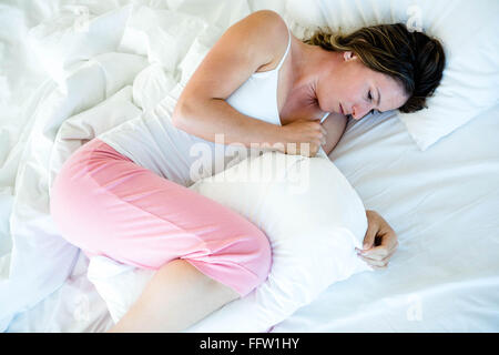 kranke Frau im Bett mit einem Kissen liegend Stockfoto