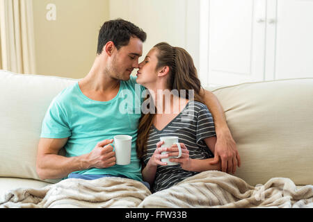 Junges Paar beim Kaffeetrinken auf Sofa kuscheln Stockfoto