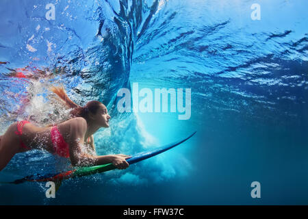 Junges Mädchen im Bikini - Surfer mit Surf Board Tauchgang unter Wasser unter großen Ozeanwelle.