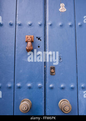 Haustür, blau, getäfelt, mit handgeformtem Klopfer, zwei Türknöpfen, einem religiösen Symbol und einem Euroschloss, Frigiliana, Malaga, Andalusien, Spanien. Stockfoto