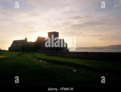 Die aufgehende Sonne über der Turm von Iona Abteikirche mit die gepflasterte Straße der Toten in den Vordergrund. Inneren Hebriden, Schottland, Vereinigtes Königreich Stockfoto