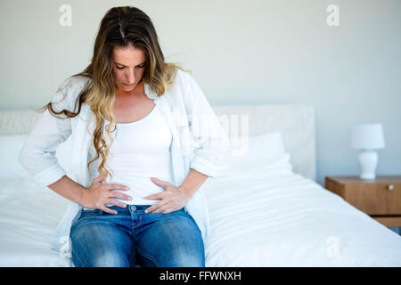 Frau sitzt auf ihrem Bett mit dem Bauch Stockfoto