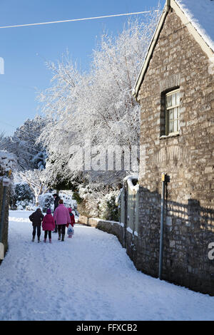 Kleine Familie, die zu Fuß durch eine verschneite Fahrspur unter einem strahlend blauen Himmel in Cowbridge, Vale of Glamorgan, Wales Stockfoto