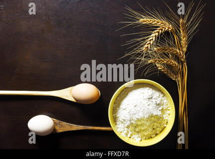 Schüssel mit Weizenmehl mit Ähren und Eiern auf hölzernen Hintergrund Stockfoto