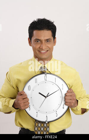 Geschäftsmann hält Wanduhr in beiden Händen vor der Brust Herr #703T Stockfoto