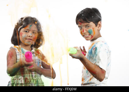 Zehn und acht Jahre alten Jungen und Mädchen, die sprühen Wasserfarben auf Glas mit Hilfe von großen Kunststoffspritze auf Holi-Fest Stockfoto