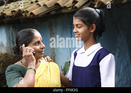 Mutter am Handy und Schule gehen Tochter vor Haus im Dorf, Maharashtra, Indien Model Release # 703Y und 703Z sprechen Stockfoto