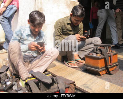Neu-Delhi, Indien. 17. Februar 2016. Die Schuh-Polierer Surender Kumar (L) und Amli spielen mit ihren Smartphones in Neu-Delhi, Indien, 17. Februar 2016. Die billigste Smartphone in Indien soll für rund 3,28 Euro, Kreuz-finanziert von der indischen Regierung in den Verkauf gehen. Indische kürzlich die USA übertroffen und hat jetzt, nach China, der weltweit zweitgrößte Smartphone-Markt. Foto: Doreen Fiedler/Dpa/Alamy Live News Stockfoto