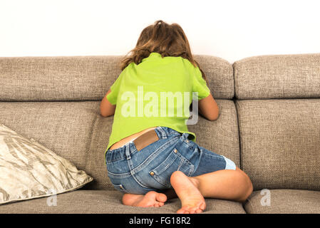 Kleines Mädchen mit dem Rücken zur Kamera auf dem Sofa zu Hause weinen Stockfoto