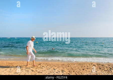 Ältere Mann im weißen Anzug zu Fuß am Strand Stockfoto