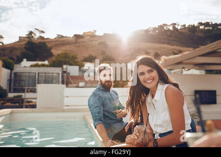 Porträt der jungen Frau mit Freunden eine Party Abend Pool sitzen. Sie lächelt und wegsehen. Junge Menschen de Stockfoto