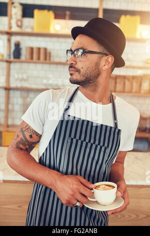 Porträt des jungen Mannes im Café am Tresen stehen und wegsehen. Männliche Barista stehen im Café mit Stockfoto