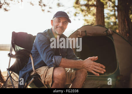 Porträt einer glücklich reifer Mann sitzt vor einem Zelt und Blick in die Kamera. Senior kaukasischen Mann am Campingplatz. Stockfoto