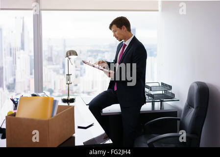 Geschäftsmann vor kurzem eingestellt für corporate Job zieht in sein neues Amt. Er nimmt einen Ordner aus einer Kiste und liest Dokumente Stockfoto