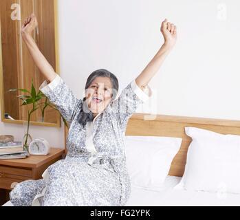 Alte Dame beide Hände dehnen und Gähnen sitzt auf Bett Herr #702S Stockfoto