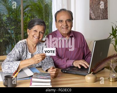 Alter Mann mit Laptop und Frau mit weißem Karton gedruckte Abstimmung auf Englisch Herr #702T; 702S Stockfoto